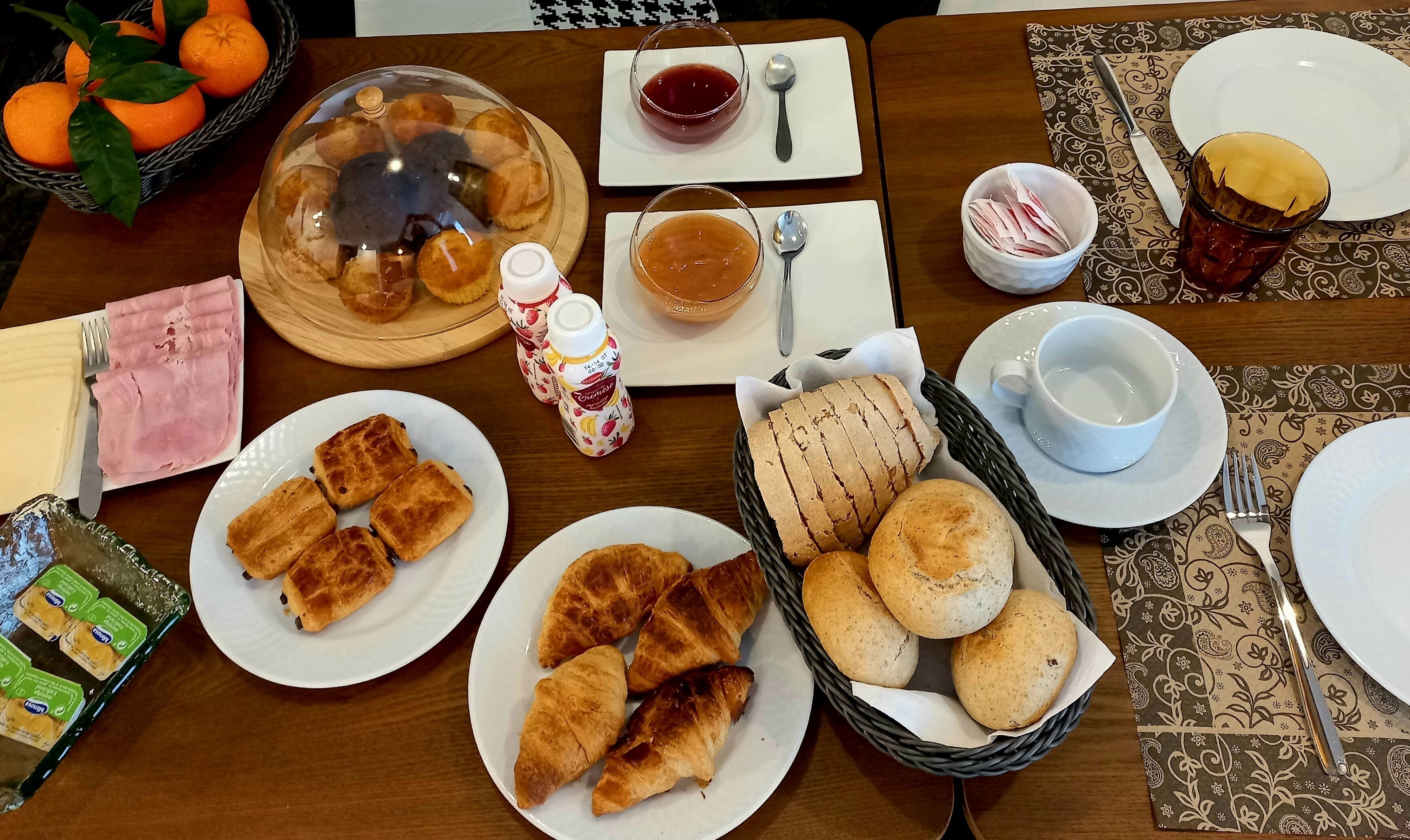 A breakfast setting with bread, pastries, and a fruit basket.