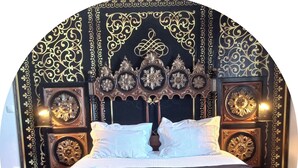 Una cama con ropa blanca, un edredón negro y dos toallas dobladas.