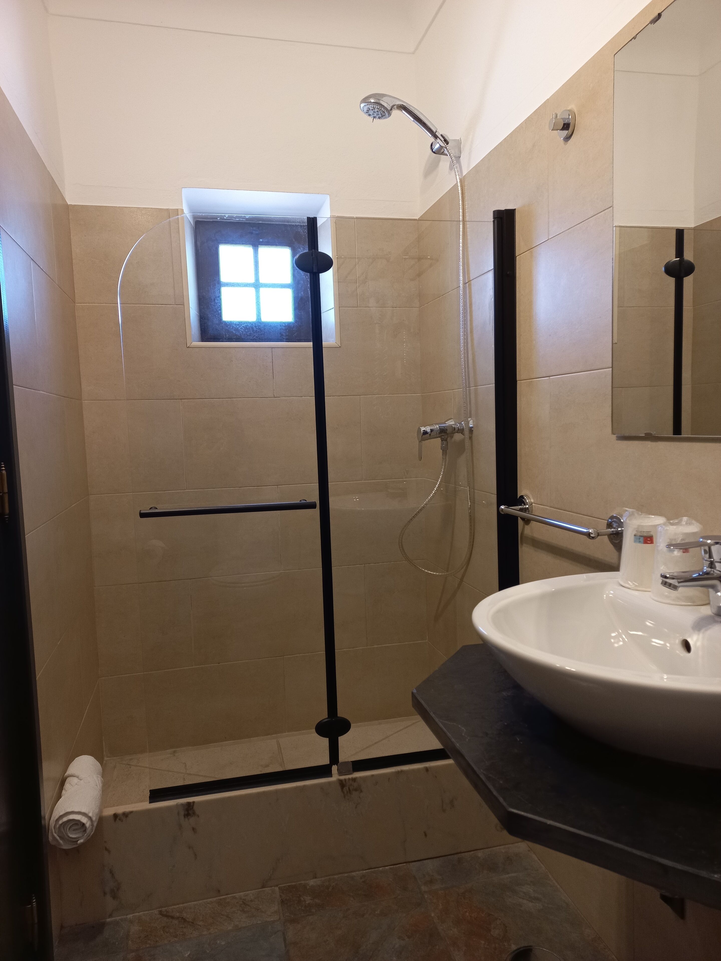 A modern bathroom with a walk-in shower, a small window, a sink, and a mirror.