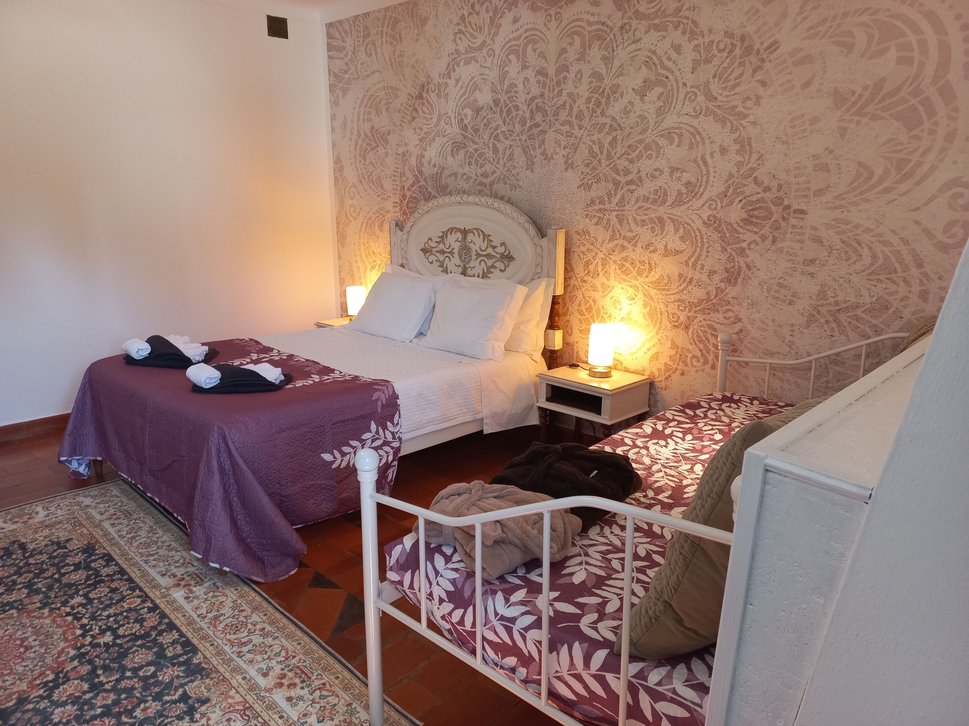 A hotel room with a bed, a nightstand with a lamp, a patterned wall, and a small rug.