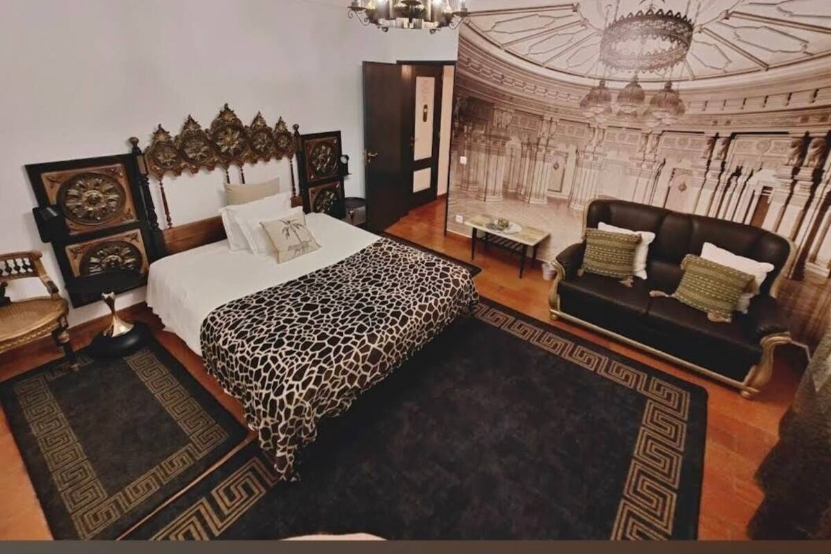 Un dormitorio con cama, sofá, candelabro y un mural en la pared.
