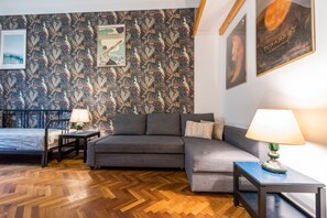 Relax in this stylish living room with a comfortable sofa, a bed, and a small table with a lamp.