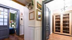 A hallway with wooden flooring, a door leading to a room with a bed, and a cabinet with glass doors. - Opera Apartments (Kraków)