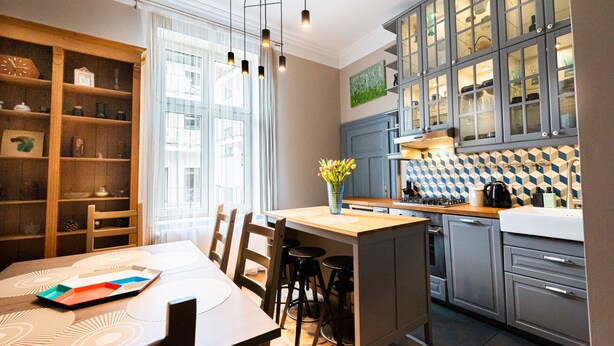 A modern kitchen with a central island, bar stools, and a dining table with a decorative tray. - Opera Apartments (Kraków)