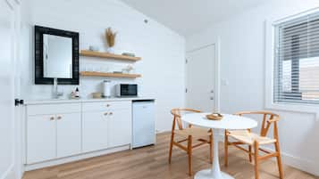 A modern kitchen with white cabinetry, a black-framed mirror, wooden shelves, and a dining area with a white table and wooden chairs.