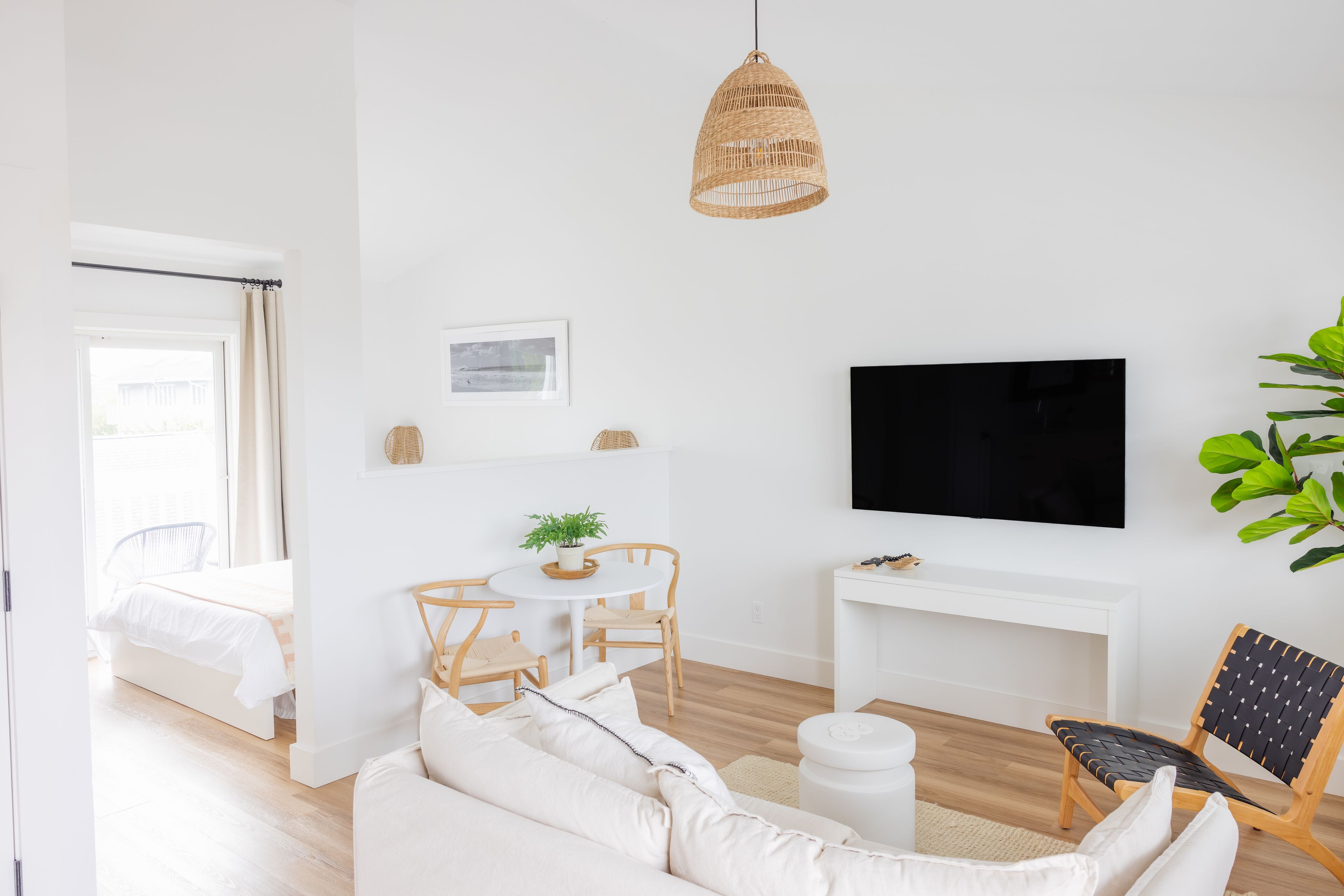 A modern living room with a white sofa, a round table with chairs, a television mounted on the wall, and a large potted plant.