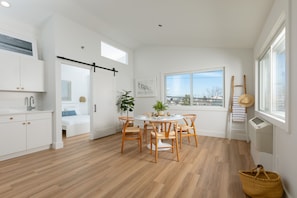 A modern kitchen with white cabinets, a dining area with wooden chairs, a large window, and a view of the city. - DUNE Fairfield Beach (Fairfield)