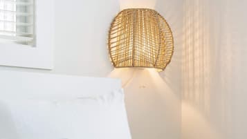 Un letto con biancheria bianca e azzurra, una lampada in vimini fissata al muro e una finestra con persiane.