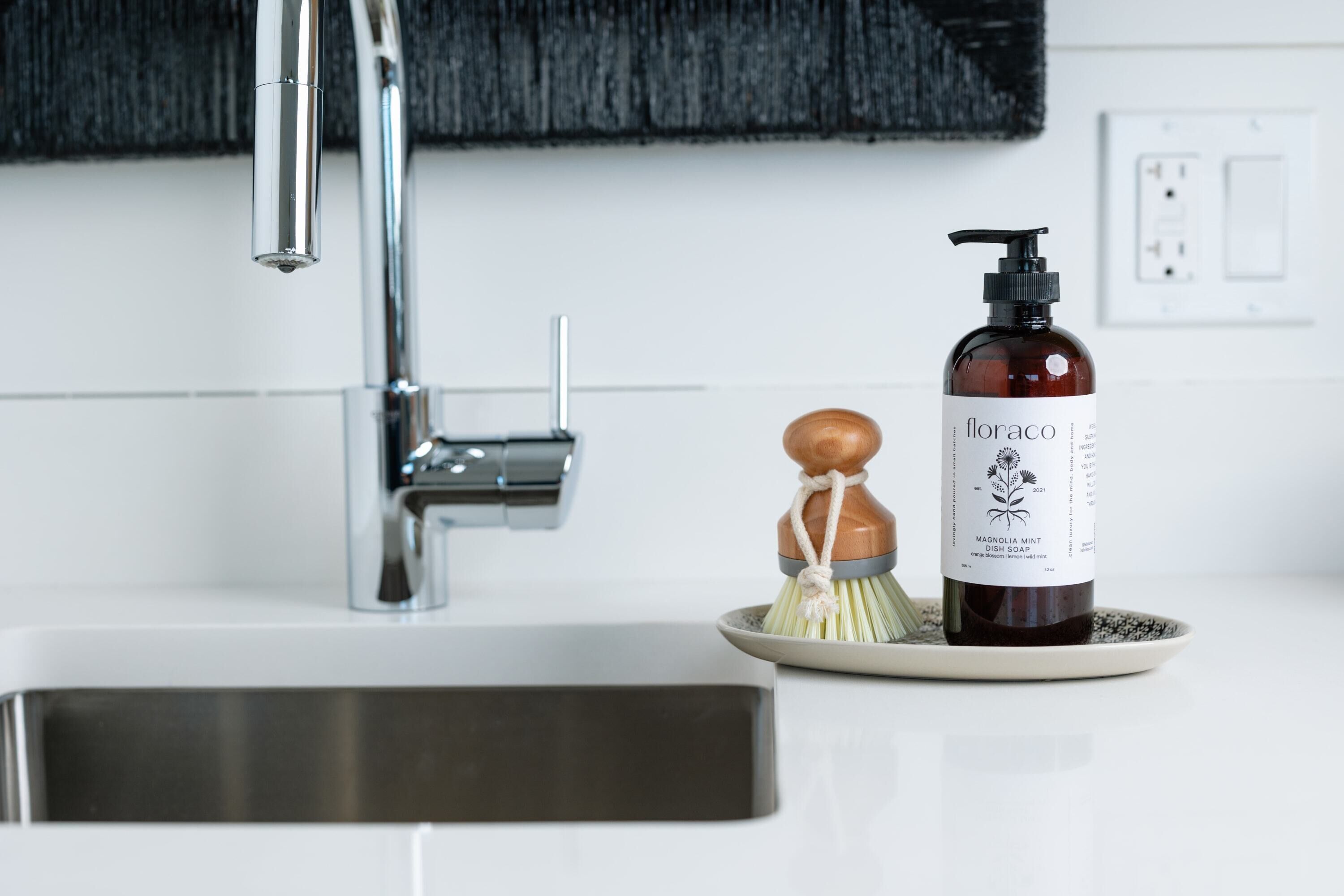 A bathroom sink with a modern faucet, a soap dispenser, and a soap dish with a brush.