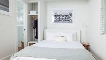 Um quarto com cama, mesa de cabeceira, armário e uma moldura na parede.