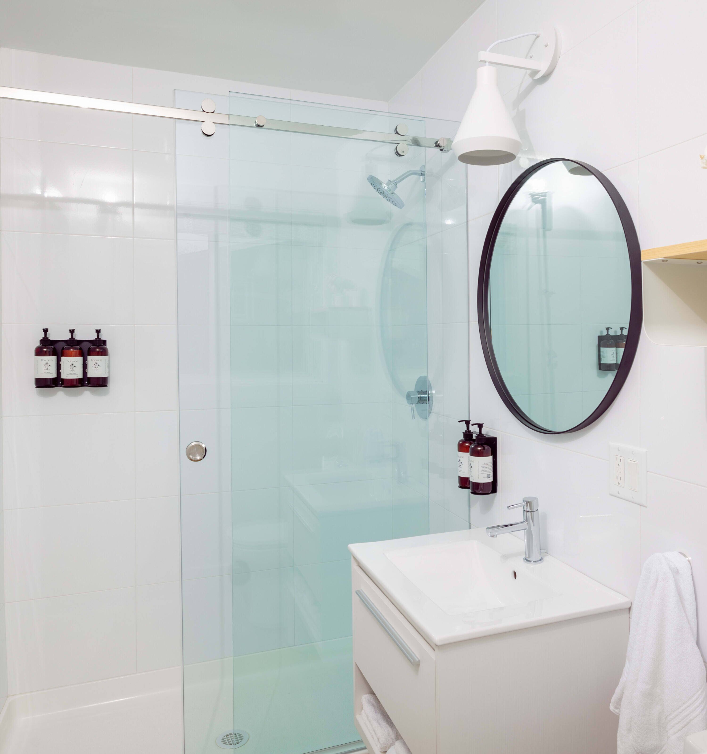 A modern bathroom with a glass shower enclosure, a white sink, and a round mirror.