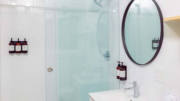 A modern bathroom with a glass shower enclosure, a white sink, and a round mirror.