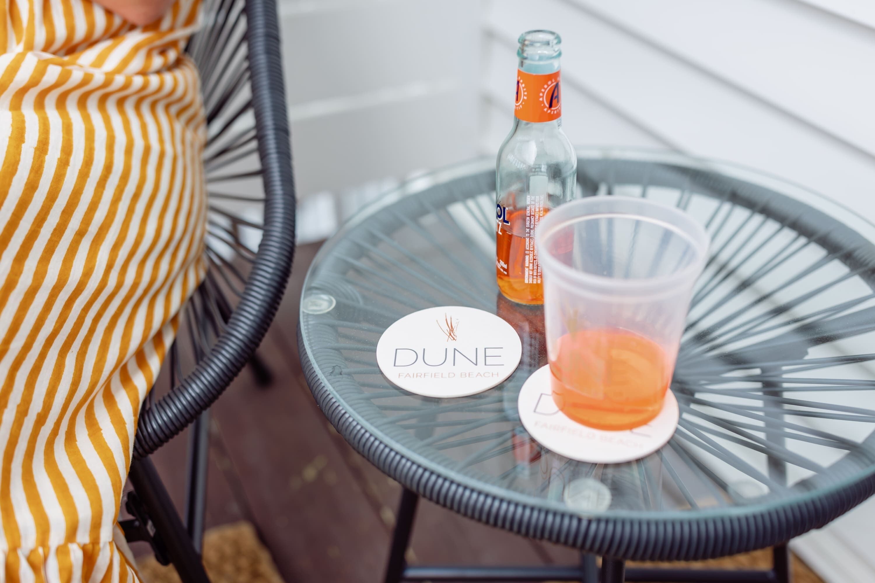 A glass table with a coaster labeled "DUNE FAIRFIELD BEACH" and a bottle of orange juice.
