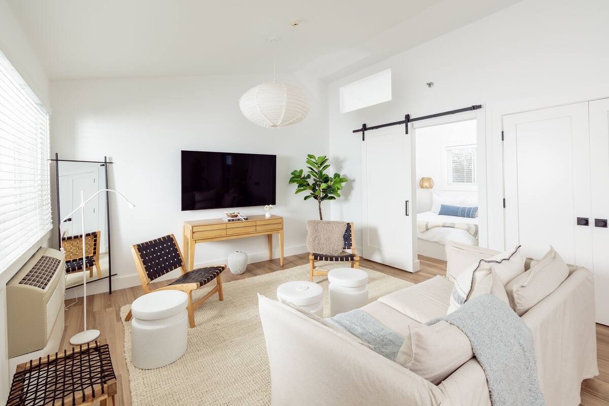 Un salon moderne avec un téléviseur à écran plat, un bureau en bois, un canapé et une grande plante.