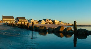 A beachfront property with multiple houses along the shore, a wooden pier, and calm waters reflecting the buildings. - DUNE Fairfield Beach (Fairfield)