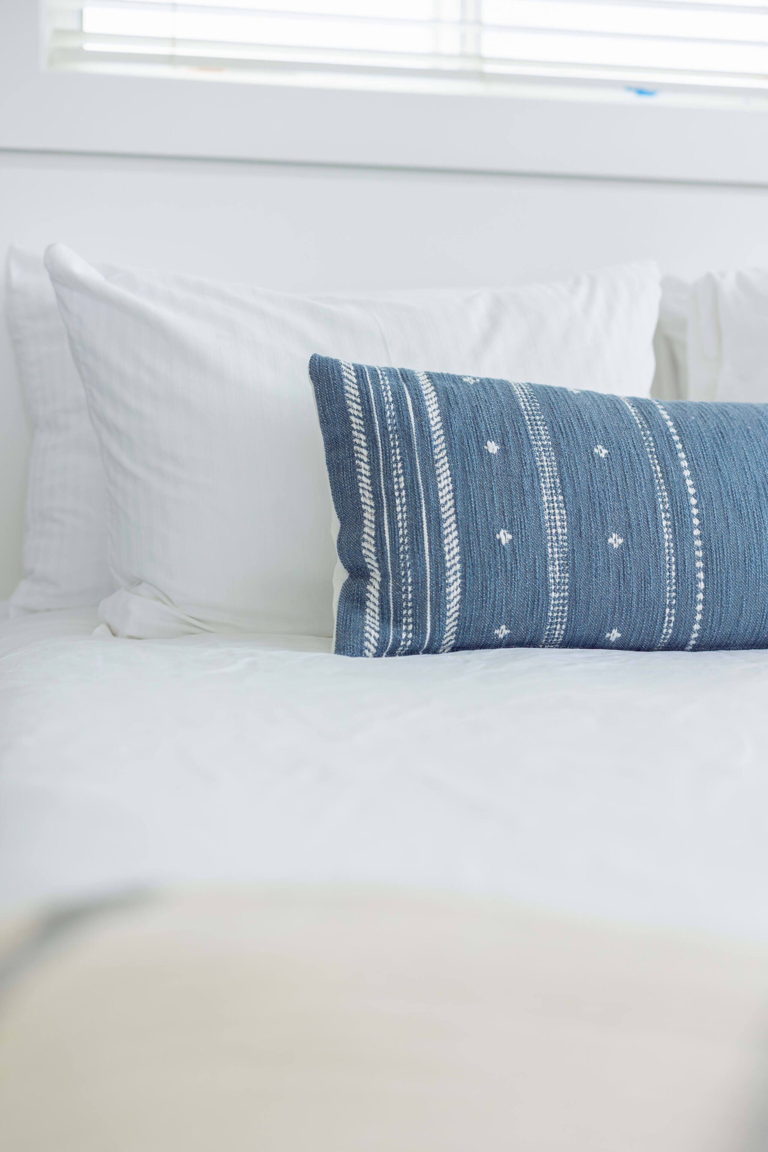 Una cama con ropa de cama blanca y una almohada azul estampada.