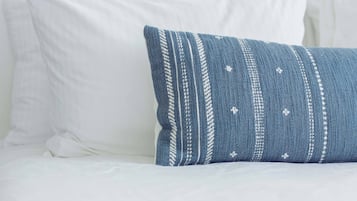 A bed with white bedding and a single blue pillow with a striped pattern.