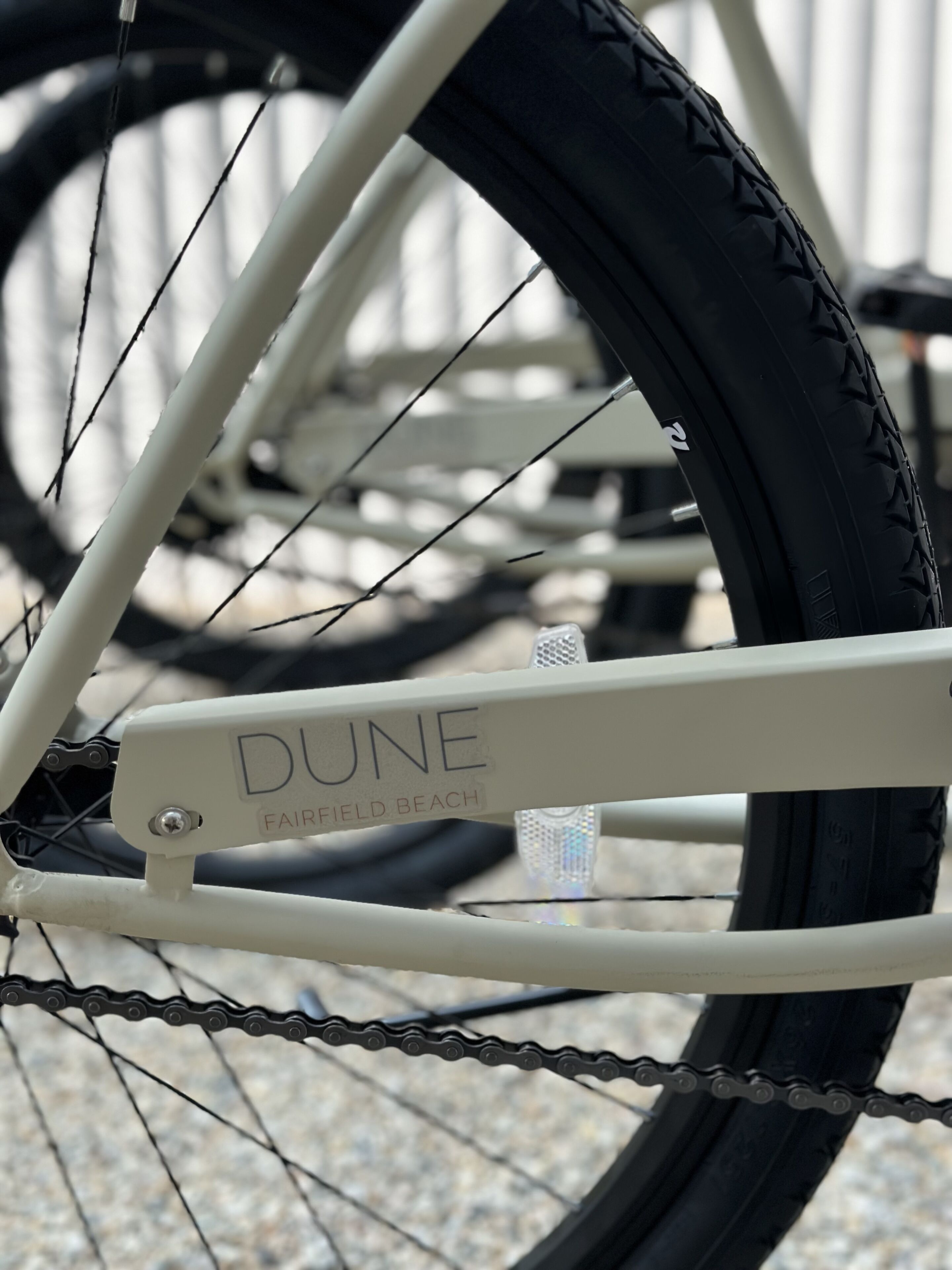 A close-up of a bicycle's rear wheel and chain, with the brand name "DUNE" and the location "FAIRFIELD BEACH" visible on the frame.
