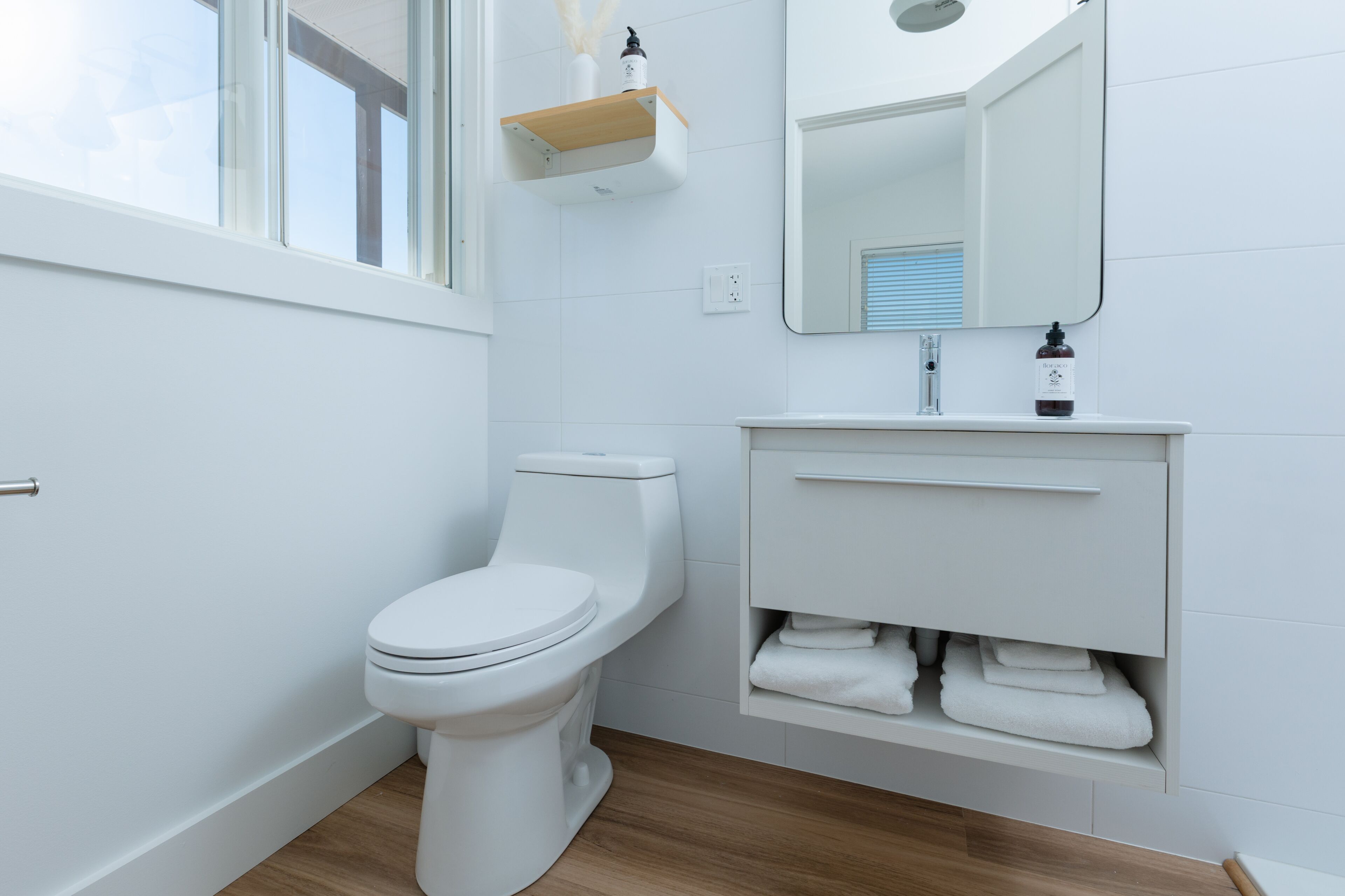 Un bagno moderno con il water bianco, un mobile lavabo con specchio e uno scaffale sopra il lavello.