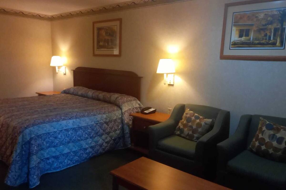 Une chambre d’hôtel avec un grand lit, deux tables de chevet, un bureau, une chaise et deux lampes fixées au mur.