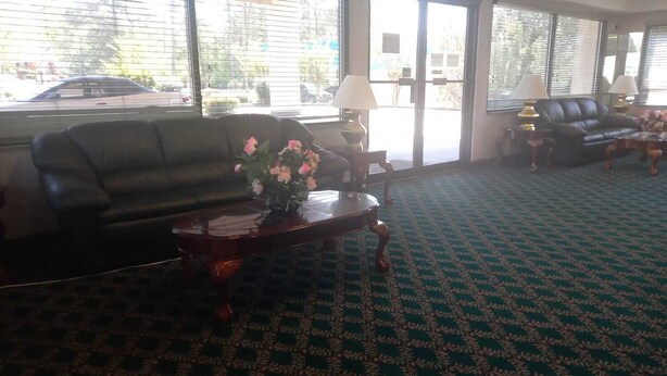 A lobby with a patterned carpet, a dark leather sofa, a wooden coffee table with a vase of flowers, and a lamp.