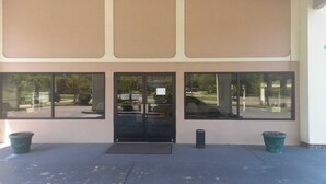 A building entrance with a glass door, large windows, and two trash bins.