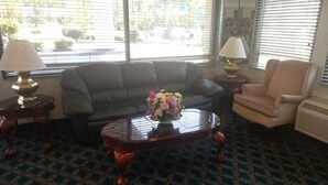 A living room with a dark leather sofa, a beige armchair, a wooden coffee table with a vase of flowers, and a lamp on a side table.