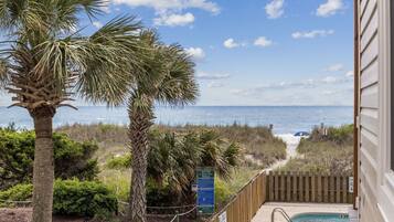 A pool area with a view of the ocean and beach, surrounded by palm trees and a wooden fence.