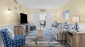 Un salon avec un téléviseur, un canapé à rayures et un tapis orné de motifs en étoile.