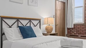 A neatly made bed with white and blue pillows, a wooden headboard, a bedside lamp, and a door to the right. - 💜Lawrenceville Loft off Butler - Top Floor & Bespoke Woodwork💜 (Pittsburgh)