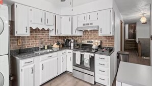 A modern kitchen with white cabinets, a brick backsplash, stainless steel appliances, and a ceiling fan. - 💜Lawrenceville Loft off Butler - Top Floor & Bespoke Woodwork💜 (Pittsburgh)