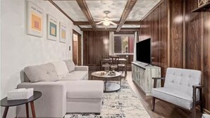 A living room with a sofa, armchair, coffee table, and a TV. There are framed pictures on the wall and a ceiling fan. - 💜Lawrenceville Loft off Butler - Top Floor & Bespoke Woodwork💜 (Pittsburgh)