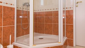 Cabina doccia con pareti in vetro, base bianca e pavimento piastrellato.