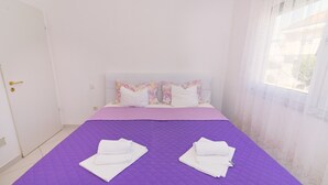 Una camera d'albergo con una coperta viola, cuscini bianchi e una porta bianca.