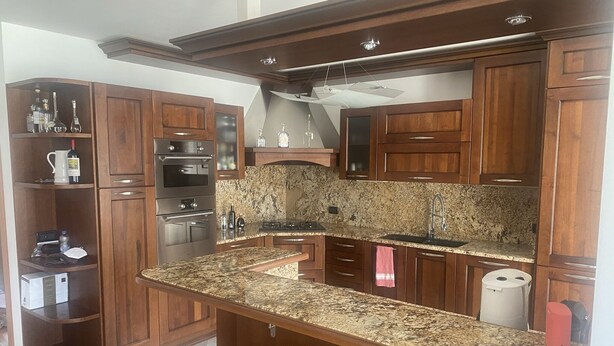 Eine Küche mit Holzausstattung, Granit Arbeitsplatten, einem eingebauten Backofen und einer Edelstahl-Dunstabzugshaube.