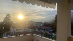 Ein Balkon mit Blick auf einen bergigen Horizont bei Sonnenuntergang, ein Fliesenboden sowie ein Holztisch und -stuhl.
