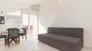 Ett vardagsrum med en grå soffa, två mönstrade fåtöljer, en tv som är monterad på väggen och ett stort fönster med persienner.