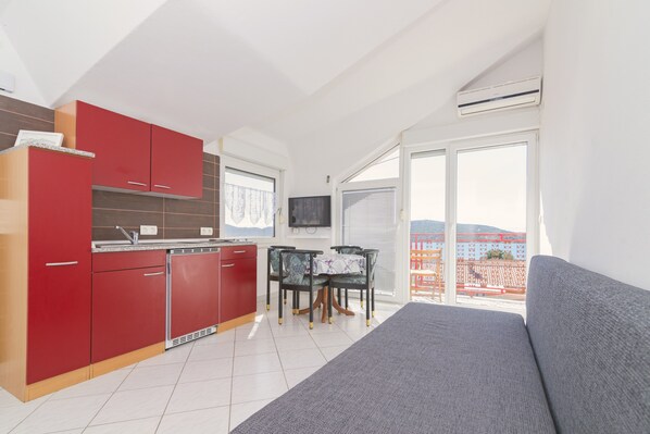 A modern kitchen with red cabinets, a dining area with a table and chairs, and a large window with a view of buildings.