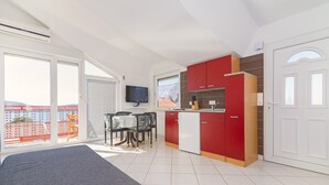 Ett modernt kök med röda skåp, en matplats med bord och stolar samt ett stort fönster med utsikt över en byggnad med rött tak.