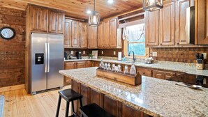 A kitchen with wooden cabinets, a stainless steel refrigerator, granite countertops, and hanging pendant lights.