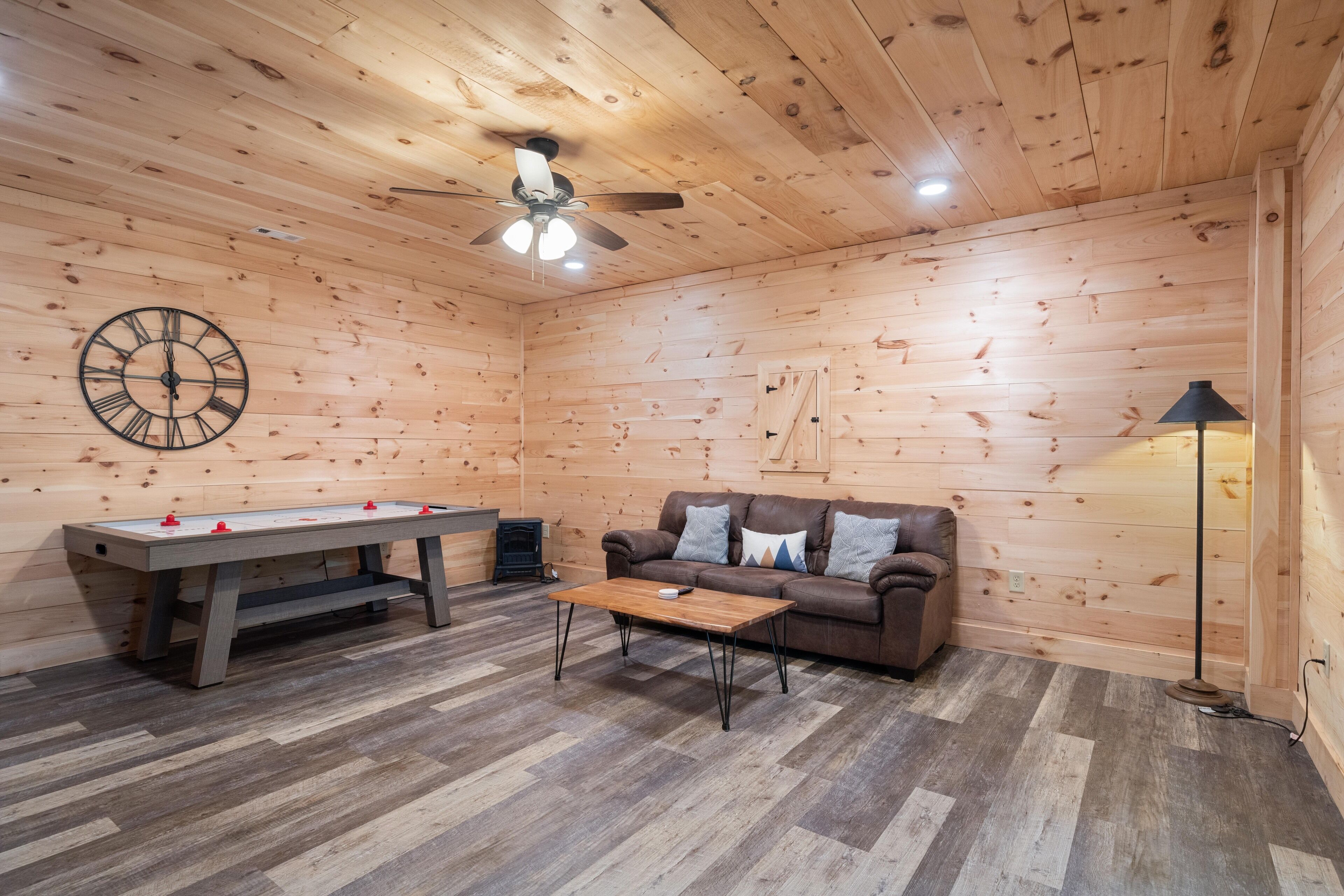 A cozy room with wooden walls, a ceiling fan, a wooden coffee table, a sofa, and a foosball table.