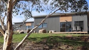 Un edificio moderno con techo plano, amplios ventanales y un área verde al frente.