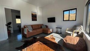Una sala de estar con un sofá modular, una mesa de centro, un televisor montado en la pared y un ventanal con vistas al desierto.