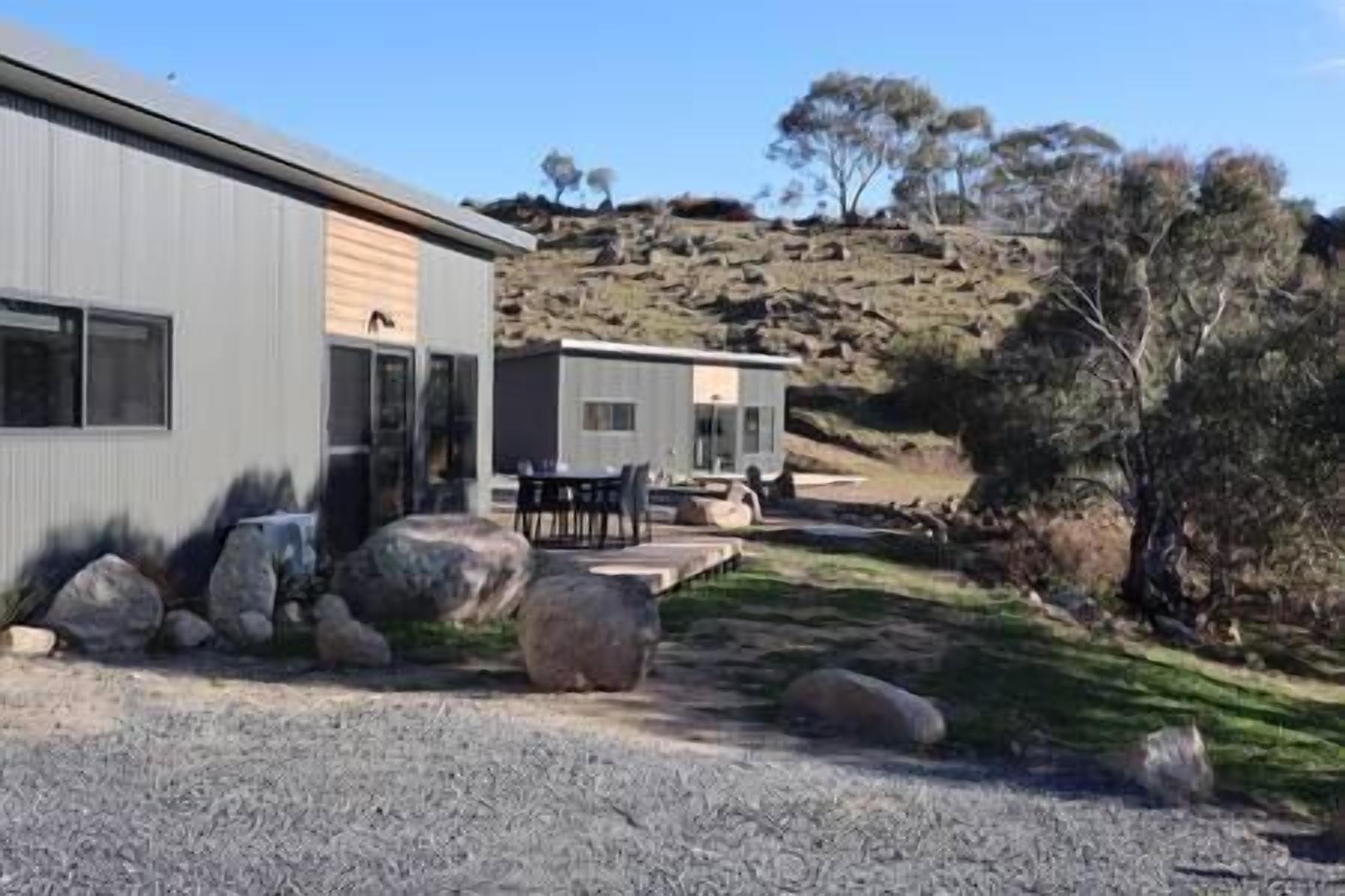 A modern building with a patio area, large rocks, and a hilly landscape with trees.