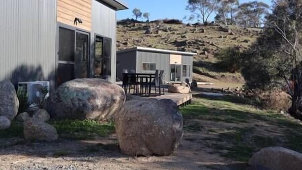 Un edificio moderno con techo plano y amplios ventanales, rodeado de rocas y vegetación escasa.