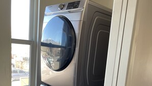 A compact laundry area with a front-loading washer and dryer, a window providing natural light, and a visible outdoor view.