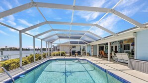 Une piscine extérieure couverte, avec une eau d’un bleu limpide, entourée de chaises longues et d’un espace patio offrant une vue sur une étendue d’eau.