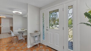 Un couloir avec des carreaux de sol à motifs, des murs blancs et une porte ornée de panneaux de vitrail.