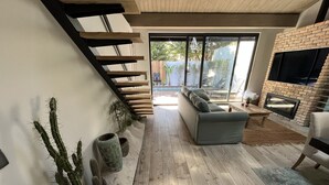 Ein modernes Wohnzimmer mit grauem Sofa, Holzboden, Kamin aus Ziegelsteinen und einer Treppe mit Holzstufen.