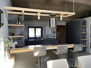 Una cucina moderna con isola centrale, sgabelli da bar, mensole in legno e una finestra con vista.